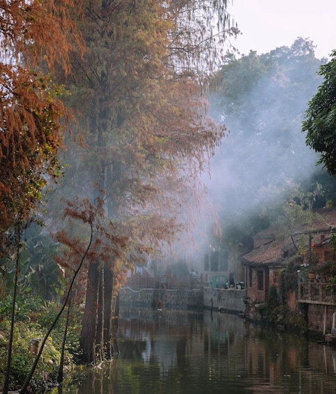 A misty river with trees and traditional buildings. 2