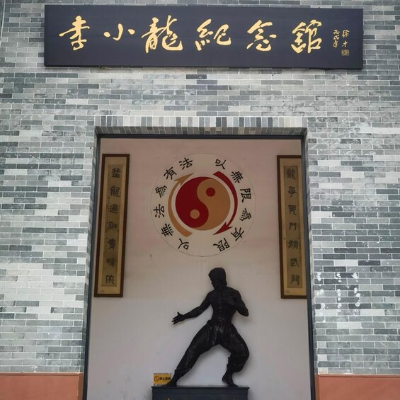 A building facade with a large black sign with gold Chinese characters, a circular emblem with Chinese text, and a statue of a person in a dynamic pose. 3