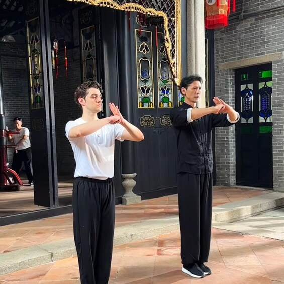 Two individuals performing a martial arts demonstration in front of a building with traditional Asian architectural elements. 4