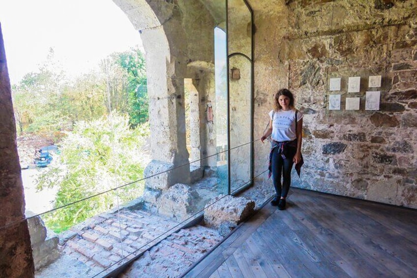 A stone interior with a person walking, a glass wall, and a wooden floor. 5