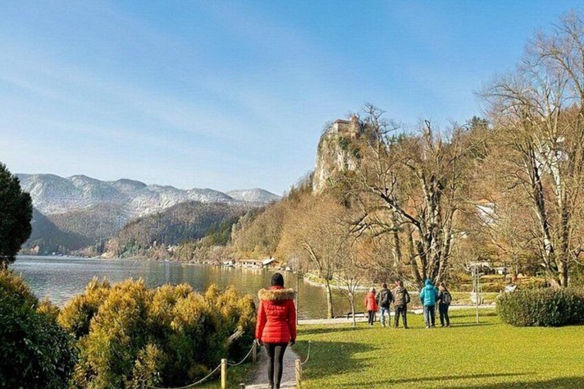 A person in a red jacket walking along a path, a group of people standing on a grassy area, and a castle on a hill in the background. 4