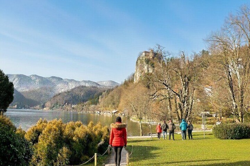 A lake with mountains in the background, a castle on a hill, and people walking on the grass. 4