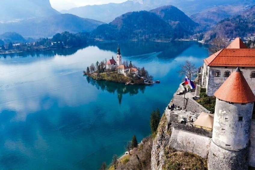 A castle overlooking a lake with a small island, a flag, and mountains in the background. 1