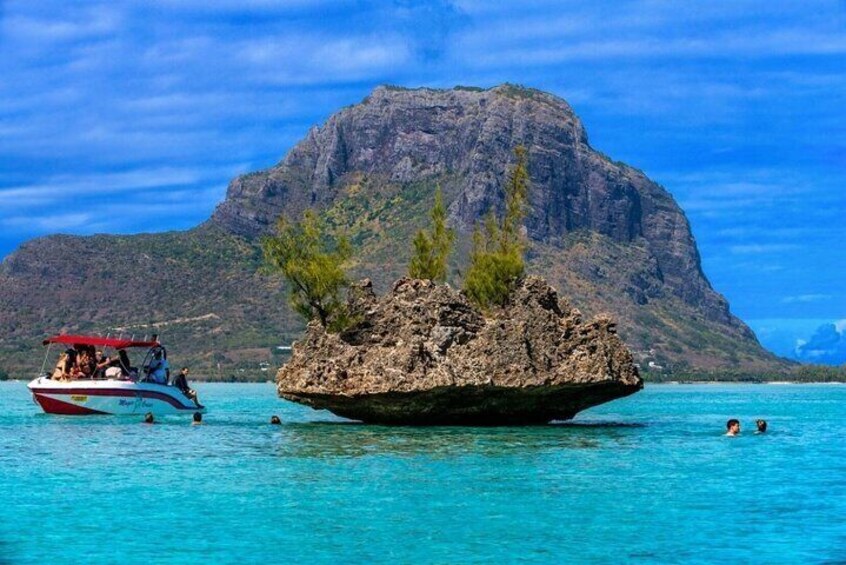 A boat on turquoise water with a rocky island and a mountain in the background. 1
