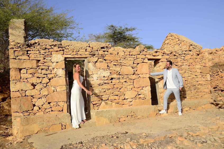 Two people standing in front of a stone building with an open doorway. 4