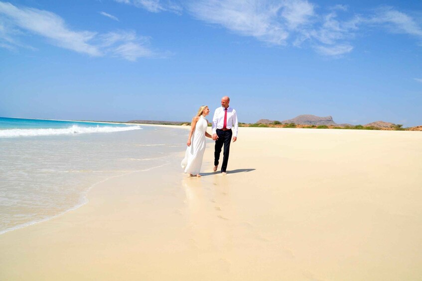 A couple walking on a sandy beach with a clear sky and distant mountains. 5