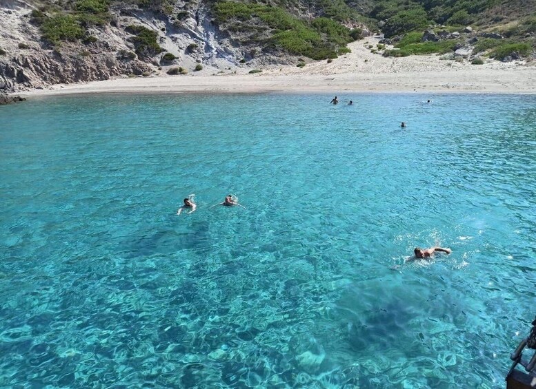 Clear turquoise water with people swimming and a rocky shoreline in the background. 4