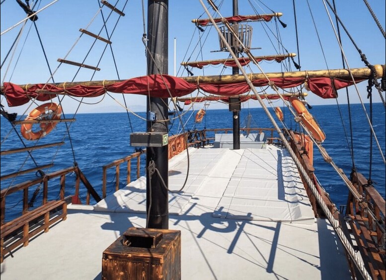 A ship's deck with wooden railings, lifeboats, and a clear view of the ocean. 3