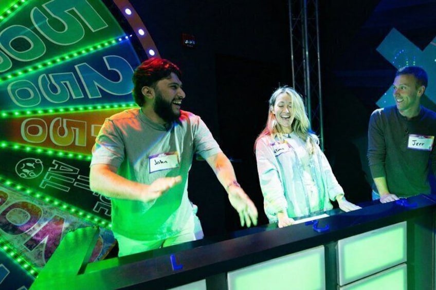 A stage with a neon sign, a man in a grey shirt, and two women. 4