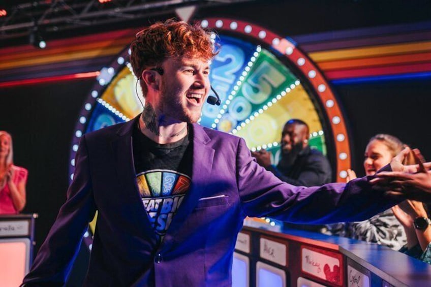 A person in a purple suit with a microphone, standing in front of a brightly lit, circular stage with a sign that reads 'SHOWTIME.' 3