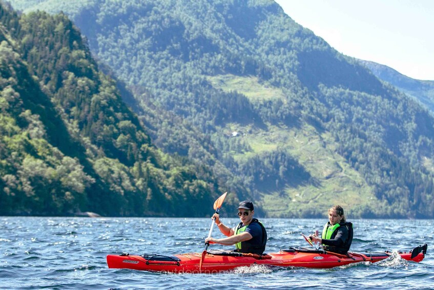 Two people kayaking on a lake with a forested mountain in the background. 2