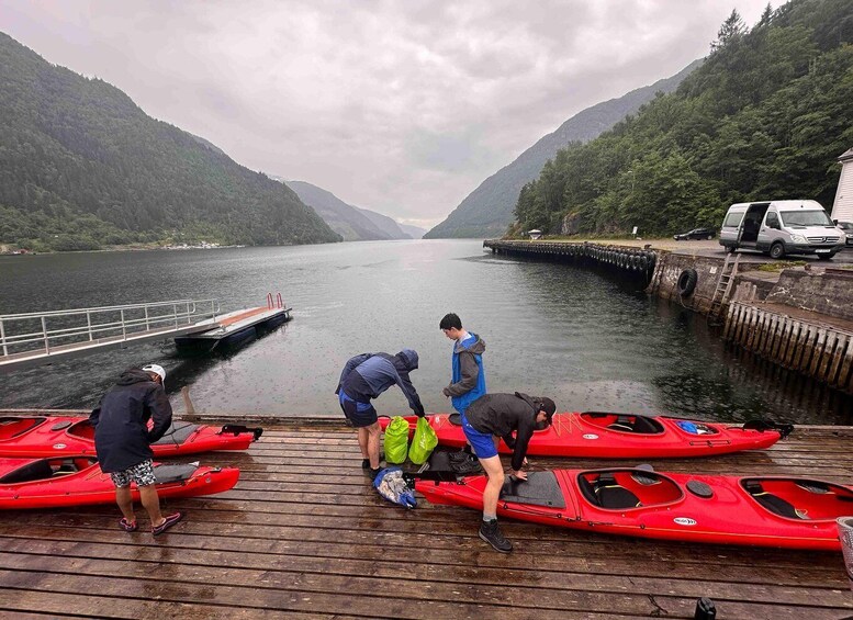 A group of people on a dock preparing kayaks by a calm lake surrounded by forested hills. 1