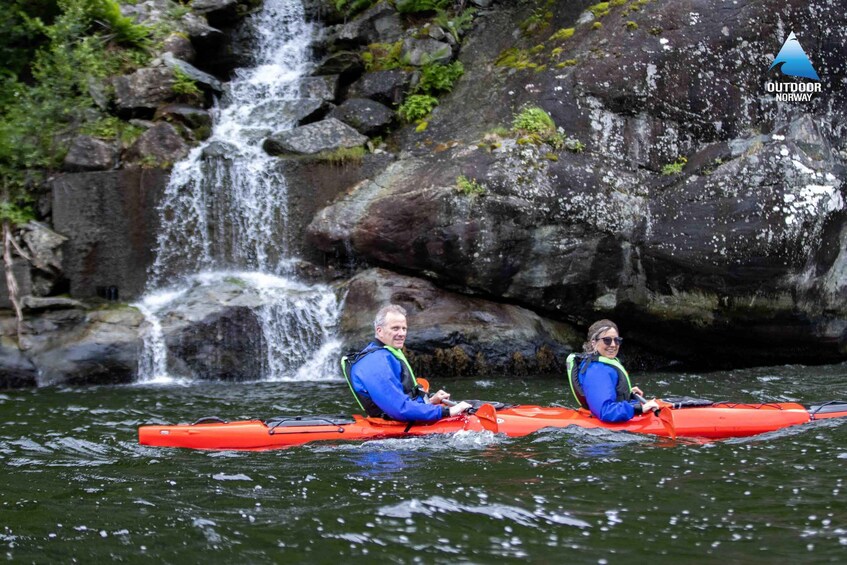 Two people kayaking on a river with a waterfall in the background. 3