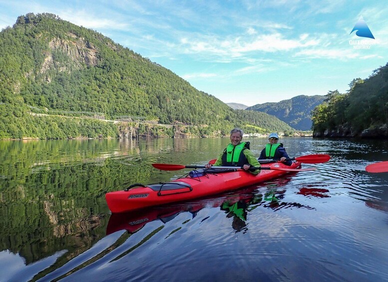 Two people kayaking on a calm river surrounded by lush green hills. 4