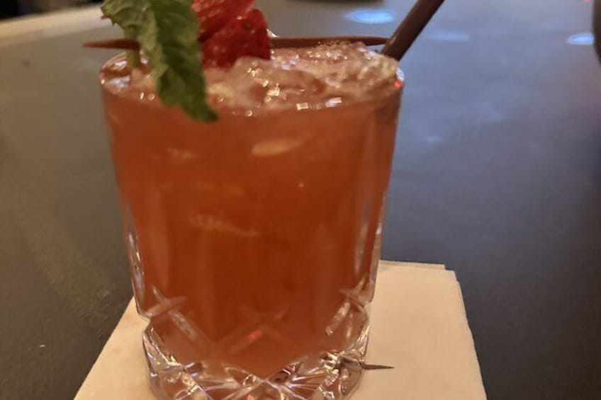 A glass of orange-colored beverage with a strawberry and mint garnish, ice cubes, and a straw on a napkin. 4