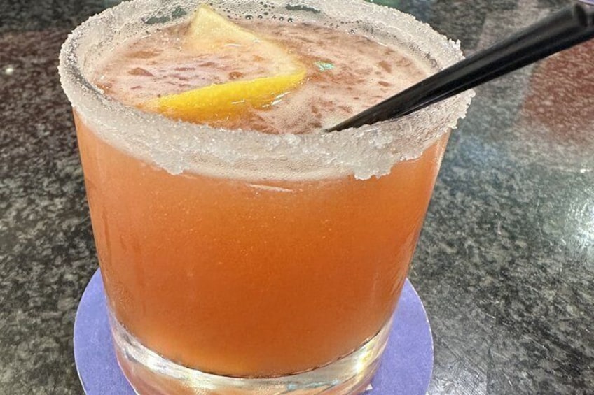 A glass with a frothy beverage, a lemon slice, and a black straw on a coaster. 3