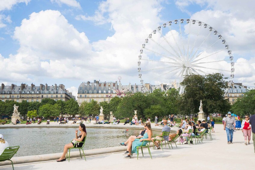 A Ferris wheel, a body of water, and people sitting by the water's edge. 5
