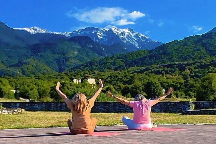 Two people sitting on a red mat outdoors with a mountainous landscape in the background. 1