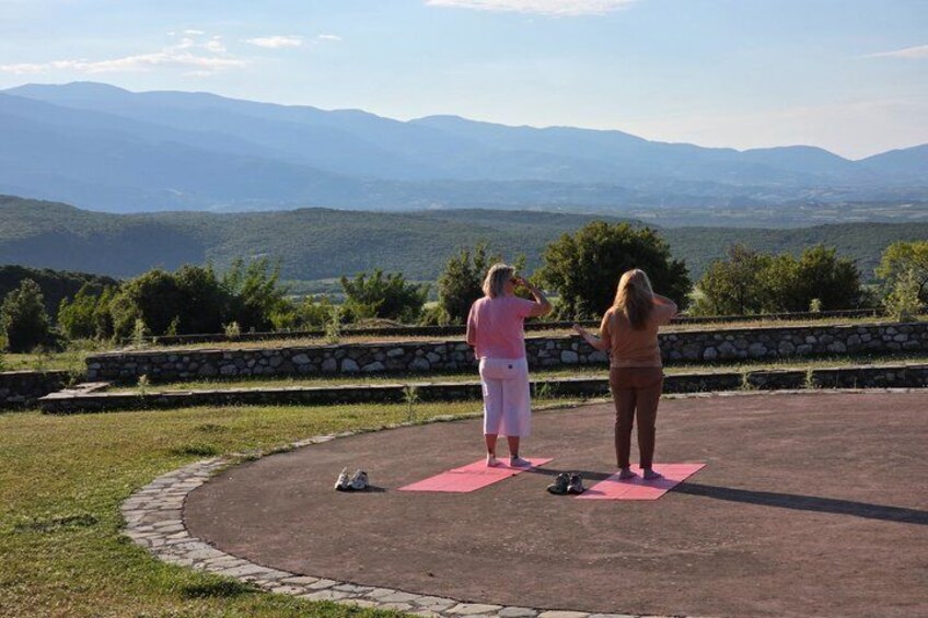 Two people on pink mats outdoors with a mountainous landscape in the background. 5