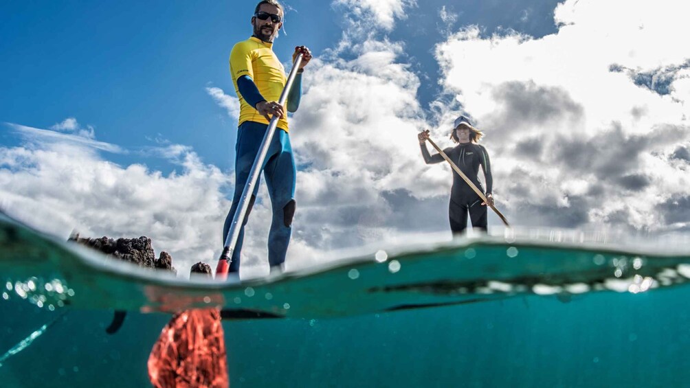 Two people standing on a boat, one holding a paddle, with a clear sky and clouds in the background. 1