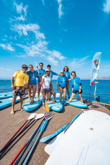 A group of people standing on surfboards by the sea, with paddleboards and paddles around them. 4