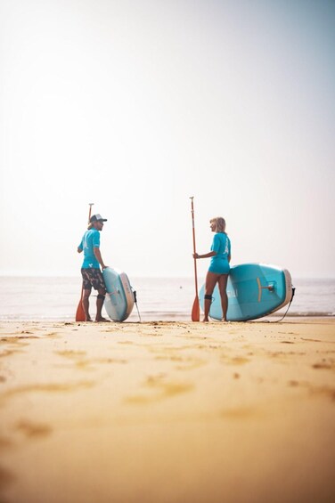 Two people on a beach with surfboards and a paddleboard. 3