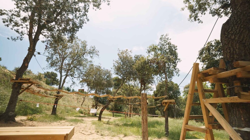 A wooden climbing structure in a natural setting with trees and a clear sky. 3
