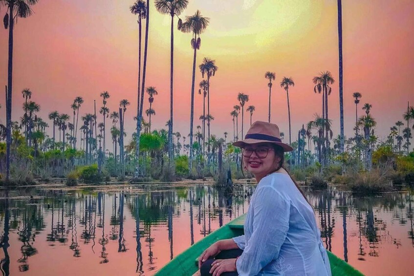 A person in a green boat on a calm water body with tall palm trees in the background and a sunset sky. 5