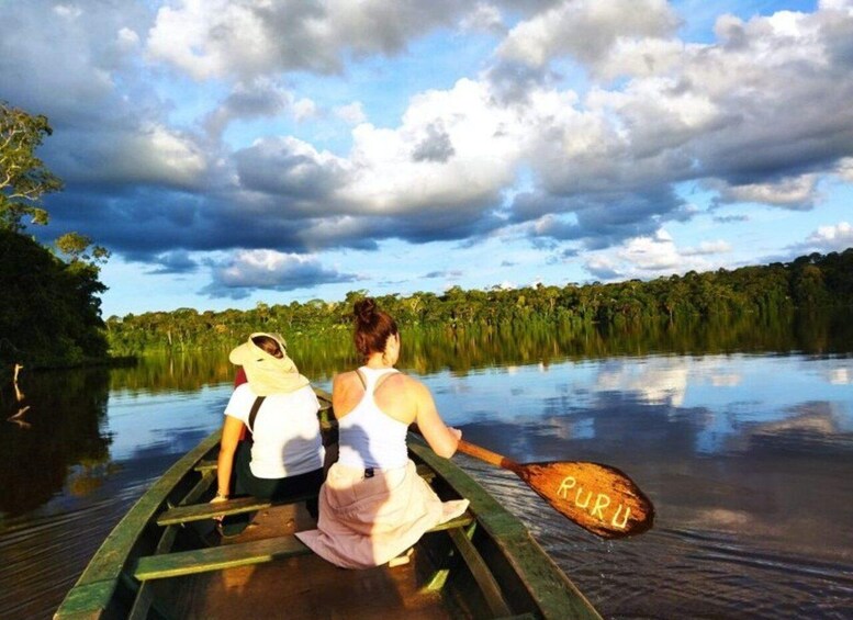 Two people canoeing on a calm river surrounded by dense forest. 1