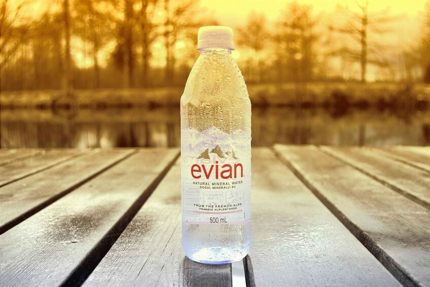 A bottle of Evian water on a wooden bench with a blurred natural background. 3