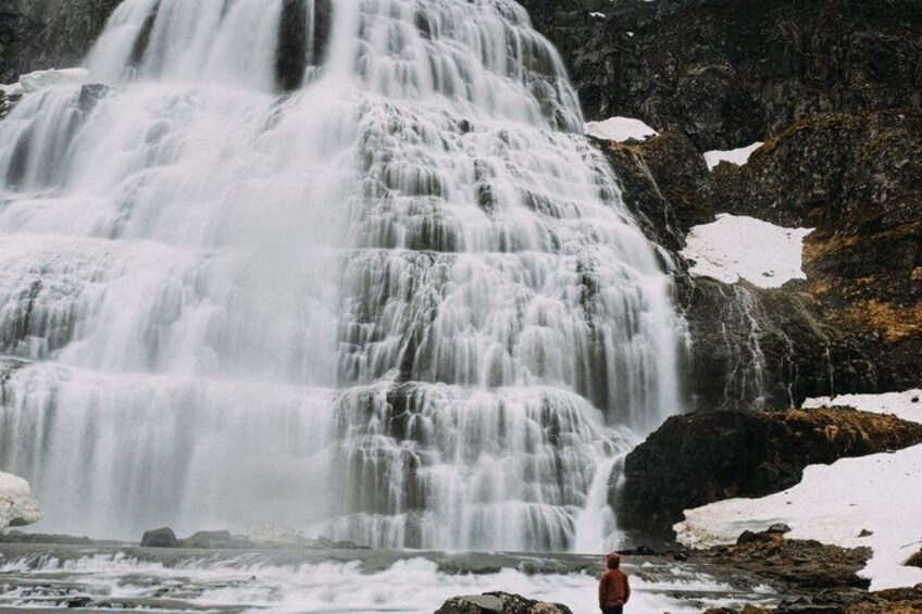 A waterfall cascading over rocks with snow patches. 1