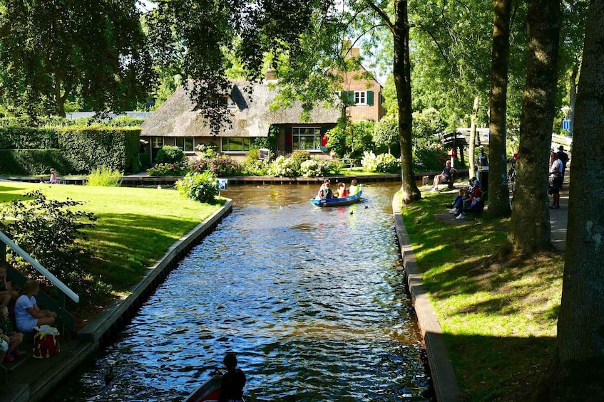 A canal with boats, people on the banks, and a thatched-roof building. 4