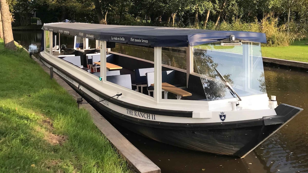 A narrowboat named 'THE RANCH II' docked at a canal with a covered seating area and tables. 1