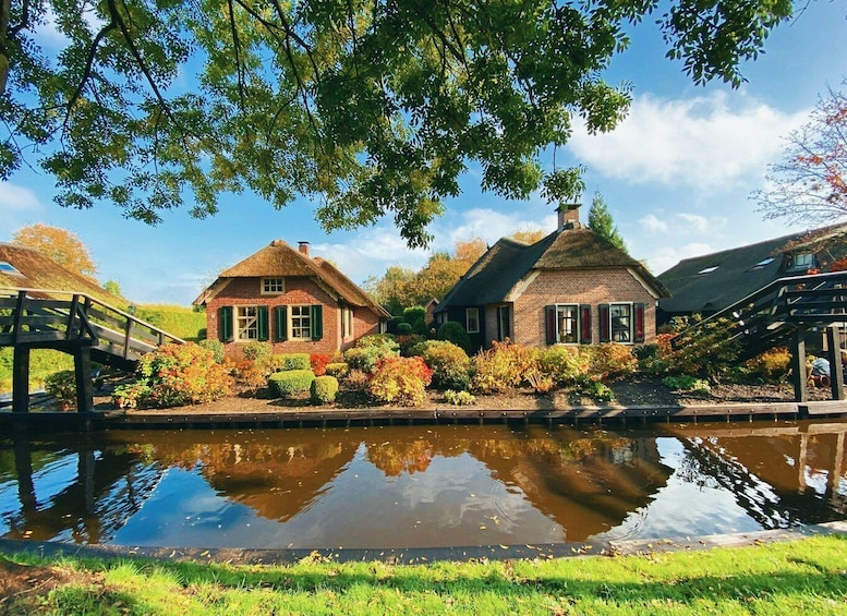A canal with two thatched-roof houses, a wooden bridge, and lush greenery. 5