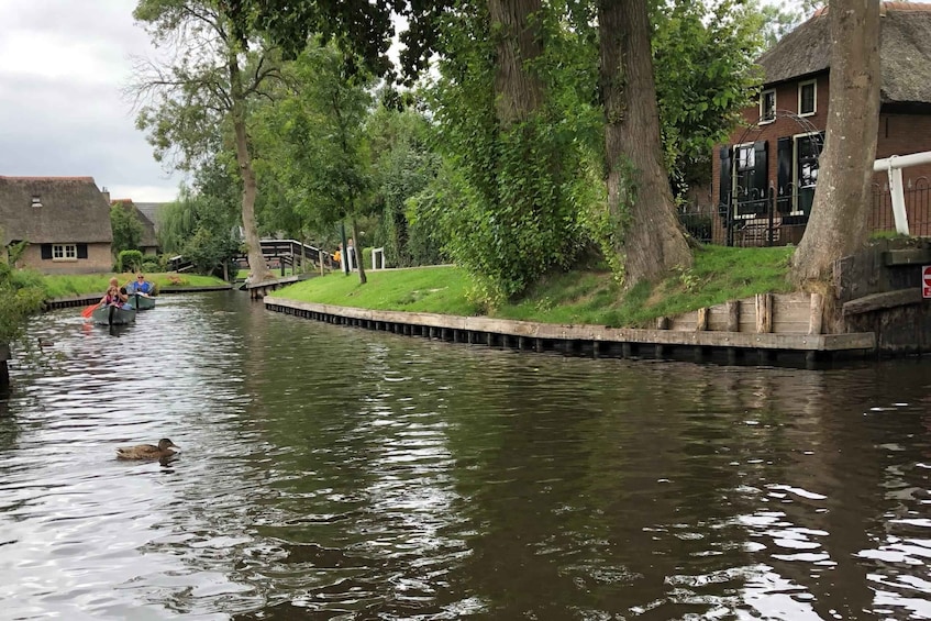 A narrow canal with a duck swimming, surrounded by trees and buildings. 2