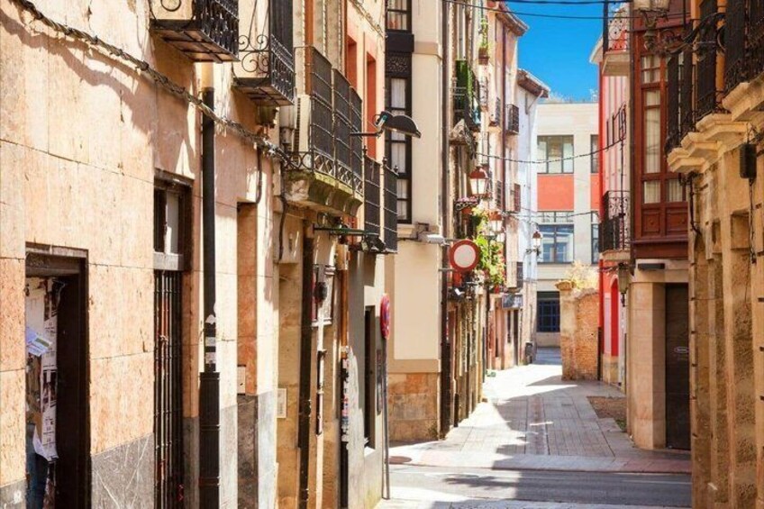 A narrow street lined with buildings, some with balconies and shutters, under a clear sky. 2