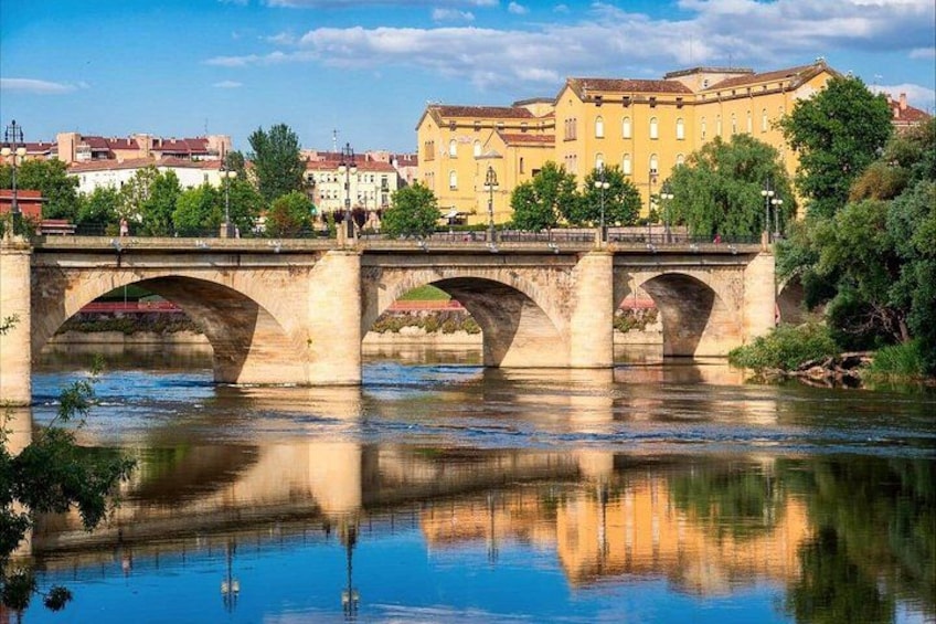 A stone bridge over a river with buildings in the background. 1