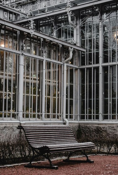 A bench in front of a greenhouse with large windows and metal framework. 3