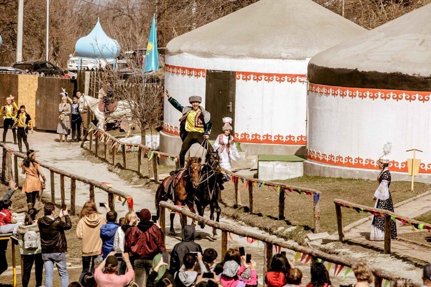 A traditional ceremony with people on horseback, a crowd watching, and yurts in the background. 3