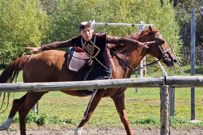 A person riding a horse, holding a reins, and passing under a wooden structure. 1