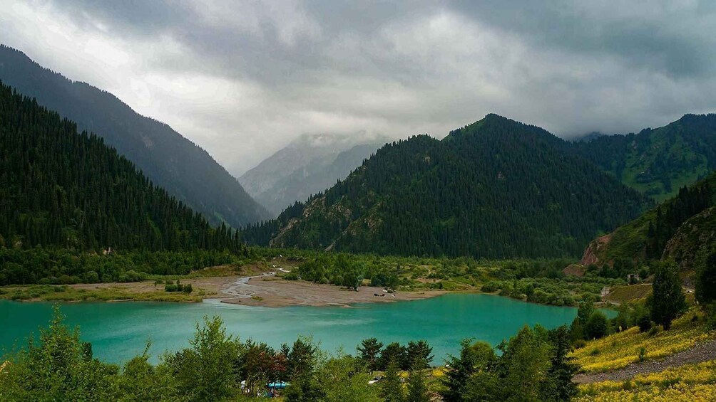 A turquoise lake surrounded by forested mountains under cloudy skies. 4