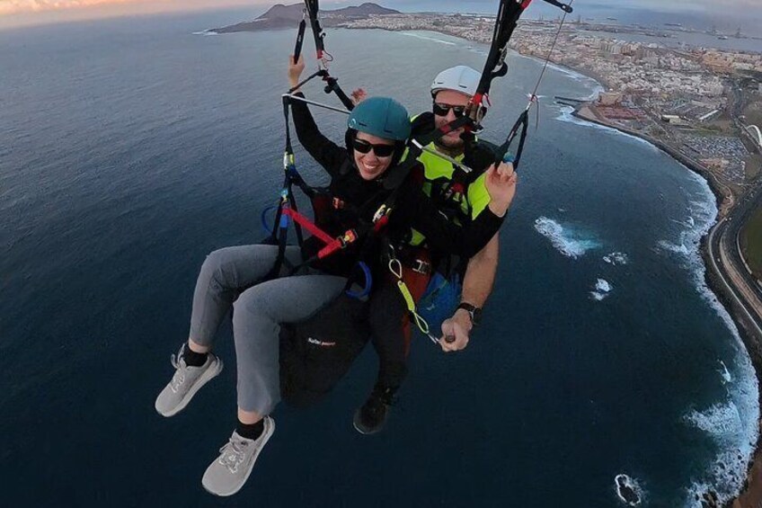 Two people skydiving over a coastal city with visible ocean waves and distant landforms. 5