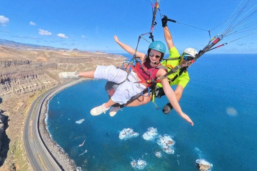 Two people paragliding over a coastal area with cliffs and a clear blue sky. 3