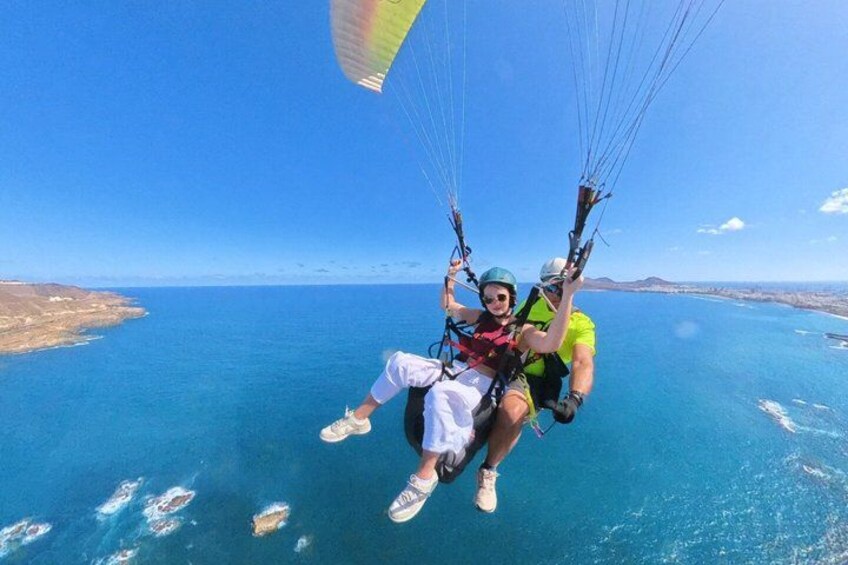 Two people paragliding over a body of water with a clear sky. 2