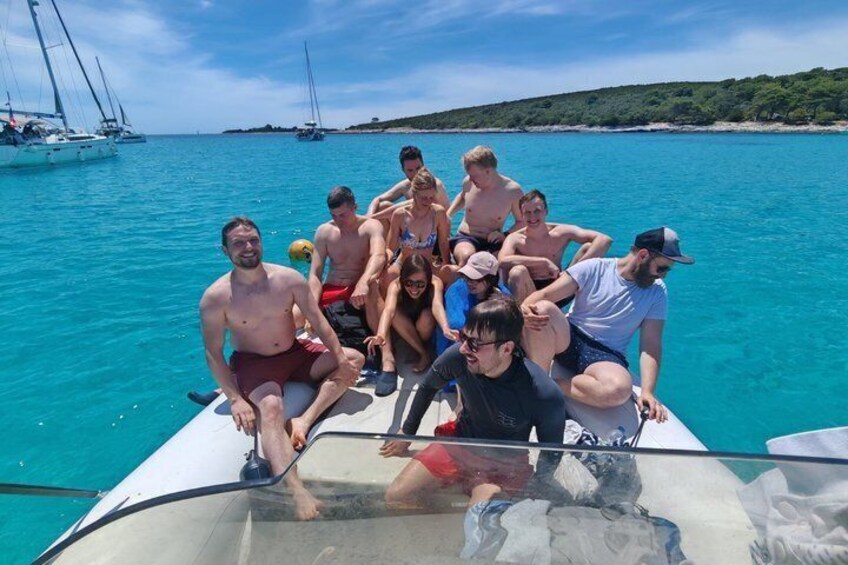A group of people on a boat with a clear blue sea and distant sailboats in the background. 4