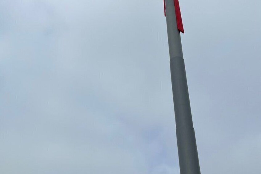 A tall, grey pole with a red flag at the top against a cloudy sky. 3