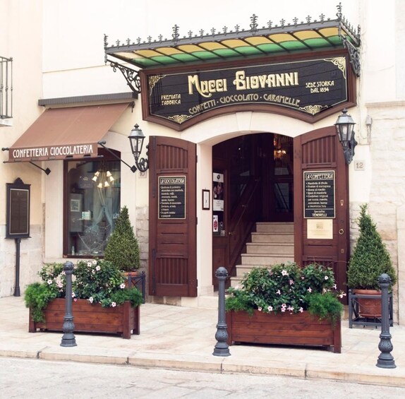 A historic building with a sign for 'Confetteria Cioccolateria' and a staircase leading to the entrance. 3