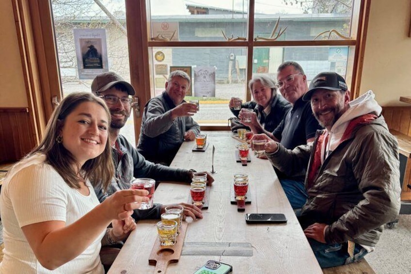 A group of people seated at a wooden table inside a building, holding glasses of beer. 1