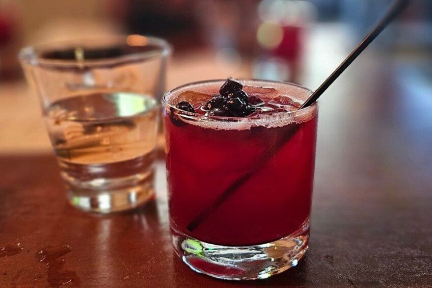 A glass of red beverage with ice cubes and a black straw, next to a clear glass of water. 3