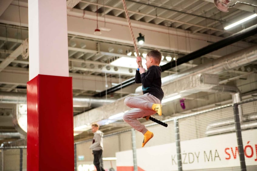 A person climbing a rope in an indoor gym with industrial ceilings and a red pillar. 2